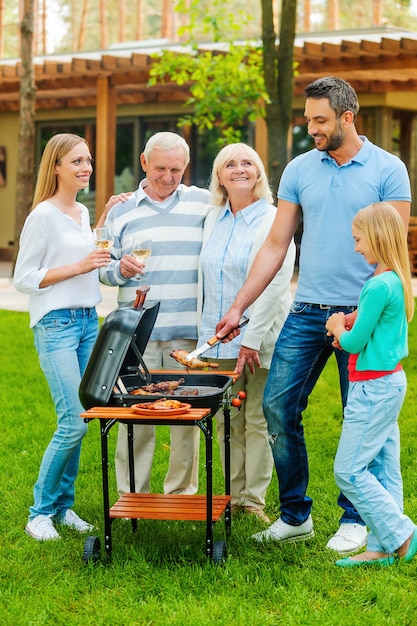 Foto hora de la barbacoa. longitud total de la familia feliz asar carne a la parrilla al aire libre