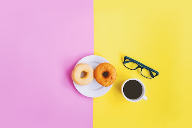 Hora del café, café negro y donuts, anteojos en fondo pastel