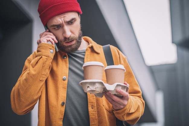 Hora de cafe. Joven barbudo con sombrero rojo sosteniendo tazas de café