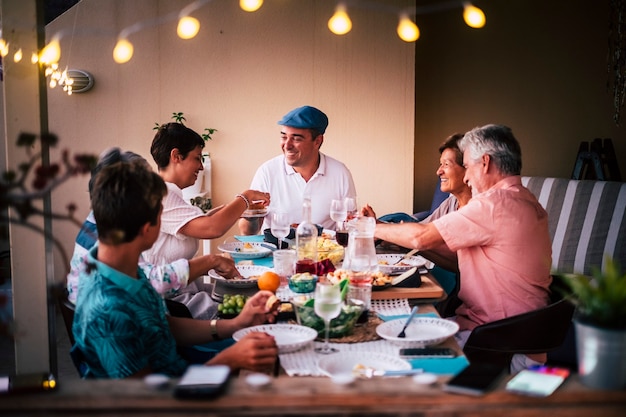 Hora de la cena en amistad con personas de diferentes edades todos juntos divirtiéndose y disfrutando de la noche con sonrisas y felicidad.