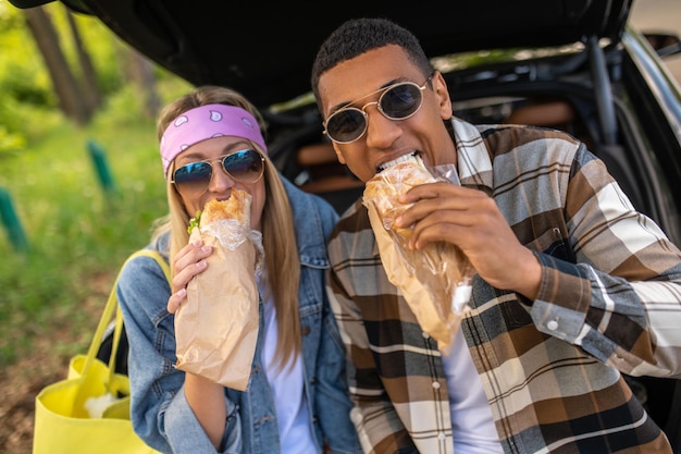 Hora de comer. Joven y mujer comiendo sándwiches y luciendo contentos