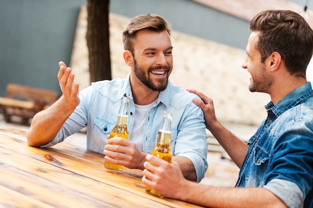 Hora da cerveja. Dois jovens alegres conversando e segurando garrafas com cerveja enquanto ficam do lado de fora