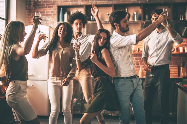 Hora da festa! jovens alegres dançando e bebendo enquanto aproveitam a festa em casa na cozinha