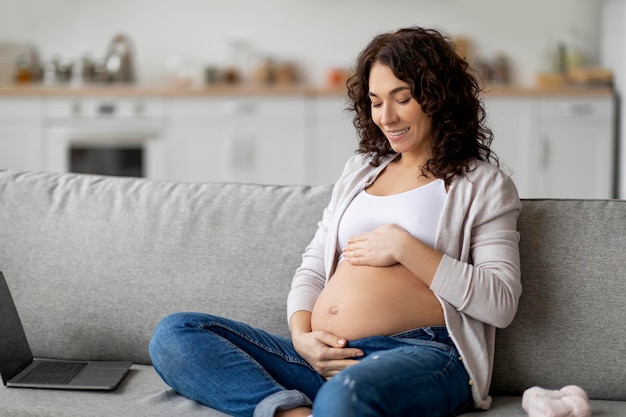 Foto hora da gravidez linda mulher grávida sentada no sofá e acariciando sua barriga