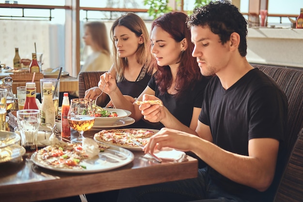 Hora da pizza. Jovens amigos desfrutando de pizza e salada em um café ao ar livre