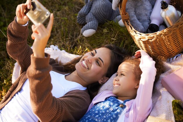 Hora da selfie. Tiro de alto ângulo de uma jovem atraente e sua filha tirando selfies durante seu piquenique no parque.