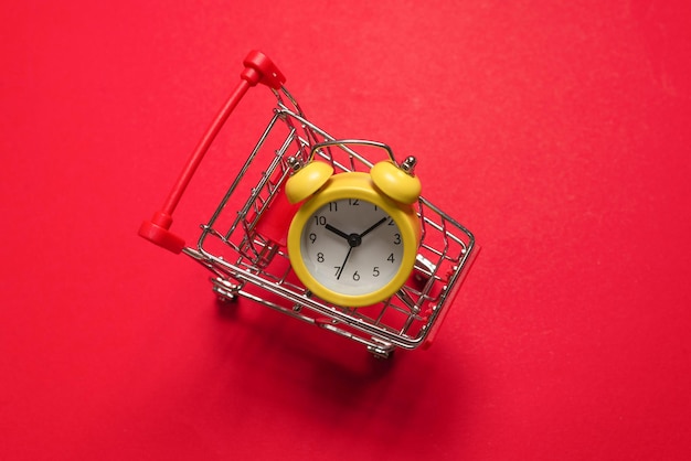 Foto hora das compras. despertador amarelo no cesto de compras em um fundo vermelho. copie o espaço.