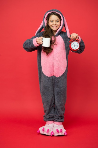 Hora de acordar Bebendo energia de café bom dia para você menina use fantasia de coelhinho da páscoa Levante cedo com uma xícara de café criança feliz em pijama kigurumi segure o despertador