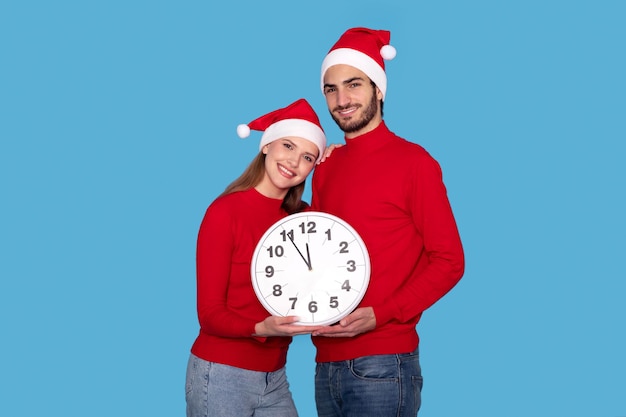 Hora de celebrar o jovem casal feliz com chapéus de Papai Noel segurando um grande relógio