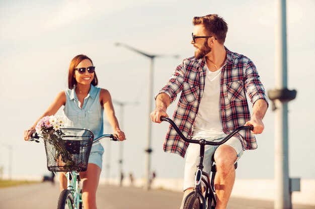 Hora de diversão. Jovem casal feliz andando de bicicleta e sorrindo