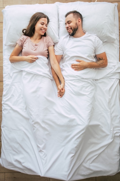 Hora de dormir. A família está dormindo. Belo jovem casal apaixonado está deitado na grande cama branca e descansando. Marido e mulher juntos na cama. Vista superior da foto