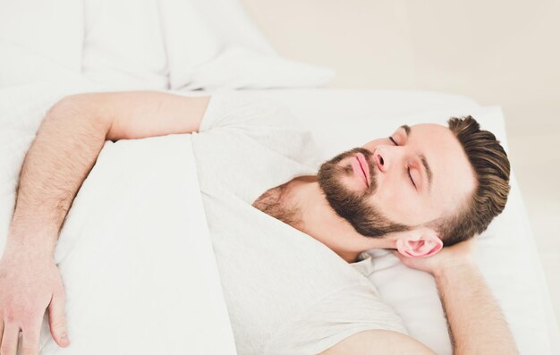 Hora de dormir e descansar Cansado homem barbudo bonito milenar dormindo descansando pacificamente na cama branca e confortável no espaço da cópia do quarto Relaxe a soneca em casa nos fins de semana