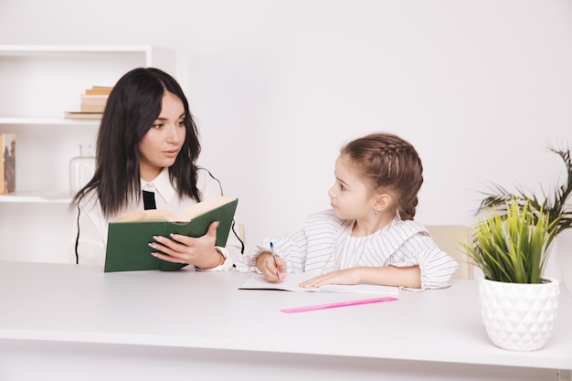 Hora de leitura de mãe e filha. aprendendo juntos, sentados à mesa.