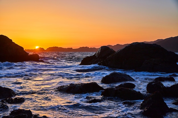 Hora de ouro do sol na praia coberta de ondas e rochas do mar