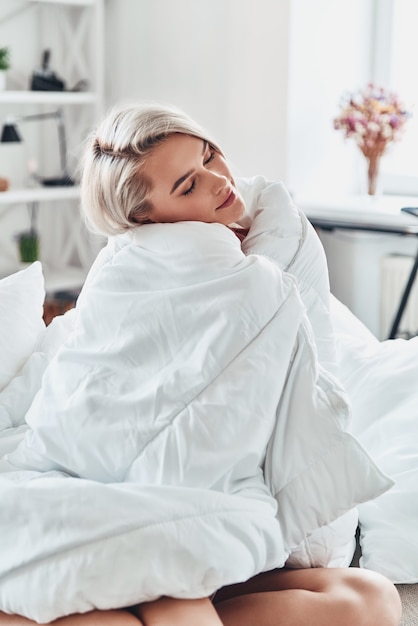 Hora de relaxar. Mulher jovem e atraente desviando o olhar enquanto se cobria com um cobertor na cama em casa