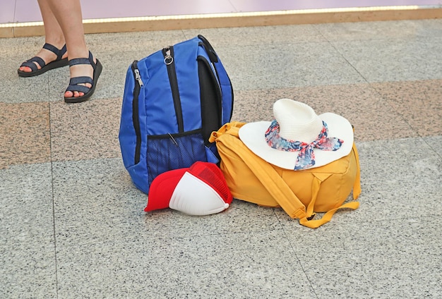 Hora de viajar chapéus de mochilas de viagem multicoloridas estão no chão da estação contra o fundo das pernas femininas