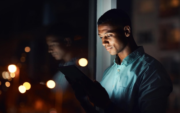 É hora de você também se conectar Foto de um jovem empresário bonito usando um tablet digital enquanto trabalhava até tarde em seu escritório