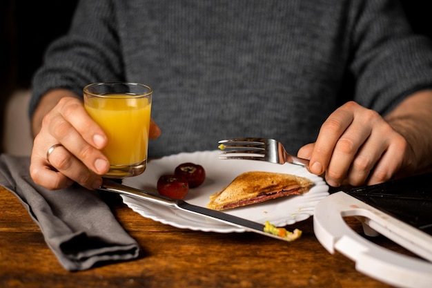 Hora del desayuno Hombre irreconocible sosteniendo un vaso de jugo de naranja El sándwich está en el plato