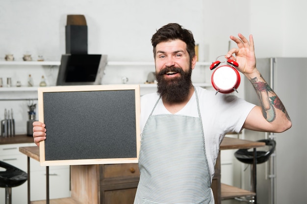 Hora del desayuno en el hotel Horario de cocina Concepto de menú Hombre feliz con espacio de copia de pizarra Servicio de catering Chef de cocina con reloj despertador Hora de comer Hora de la cena Almuerzo Cocinero hipster