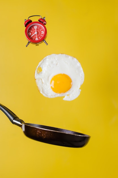 Hora del desayuno. Un huevo frito y una sartén con un reloj levitan en el aire