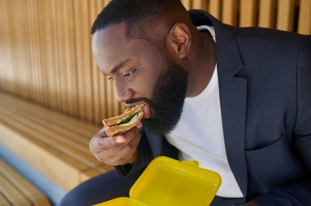 Hora do almoço. um snadwich de homem moreno com grande apetite