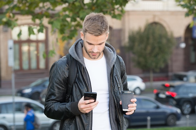 Hora do café a qualquer hora Homem bonito segura smartphone e xícara de café Café para viagem Jovem empresário bebe café para ir Estilo de vida móvel Vida moderna Nova tecnologia