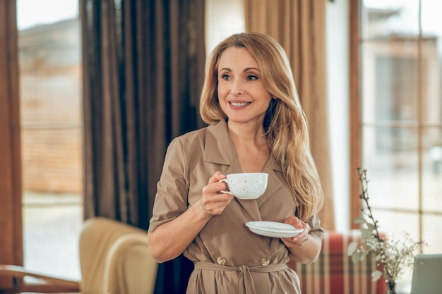 Hora do chá. mulher elegante de cabelos compridos tomando chá e parecendo satisfeita