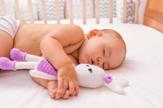 Hora de dormir. El bebé duerme con su juguete favorito, un conejito de punto, en la cama de los padres. Enfoque selectivo en la cara del niño.