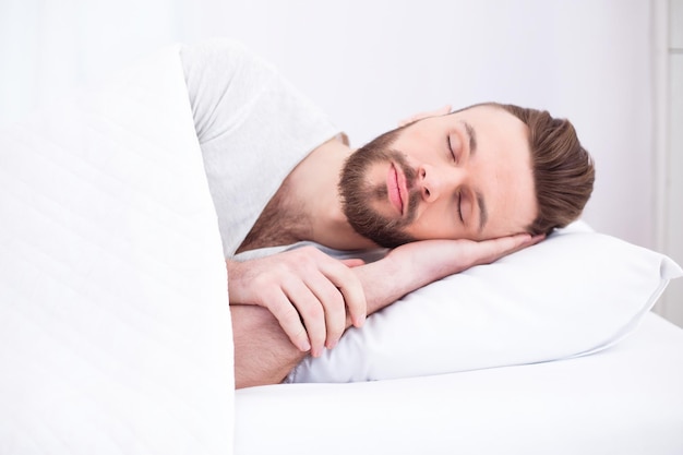 Hora de dormir y descansar Cansado milenario apuesto hombre barbudo dormido descansando pacíficamente en una cómoda cama blanca en el espacio de copia del dormitorio Relájese siesta en casa los fines de semana