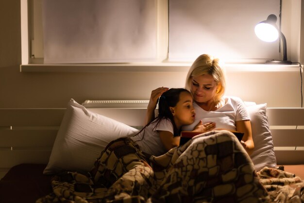 Hora de dormir en familia. Hija de mamá e hijo leyendo un libro en la cama