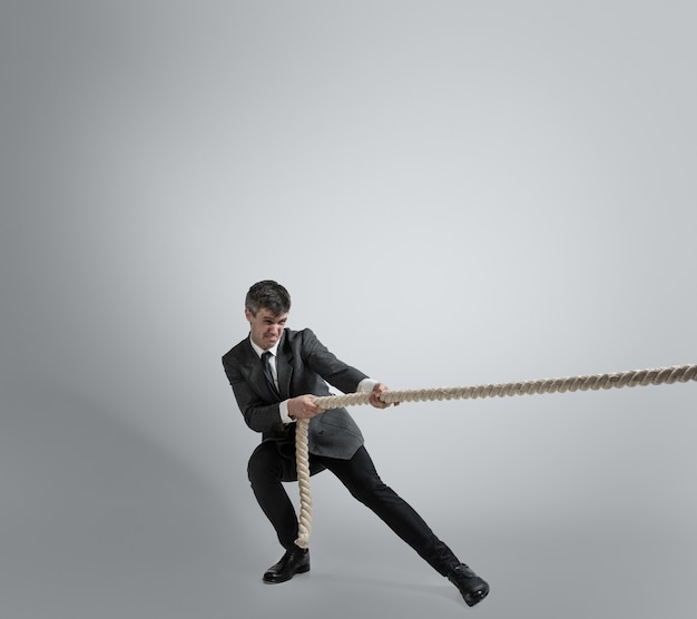 Hora de la fuerza. Hombre en ropa de oficina entrenando con cuerdas en la pared gris. Consigue objetivo, superando problemas, plazos. Hombre de negocios en movimiento, acción. Deporte, estilo de vida saludable, trabajo.