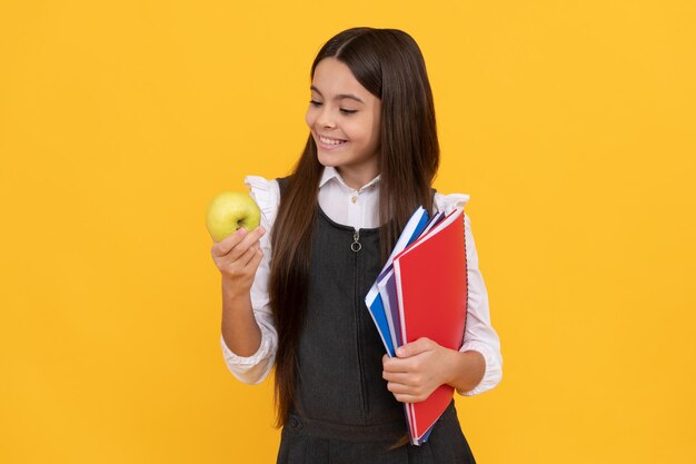 Foto hora de la merienda niña feliz mira manzana sosteniendo libros escolares merienda escolar educación alimentaria regreso a la escuela