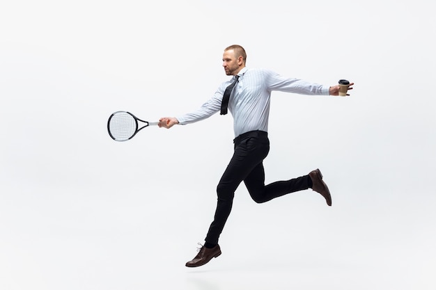 Hora de moverse. Hombre en ropa de oficina juega tenis aislado sobre fondo blanco de estudio. Formación de empresario en movimiento, acción. Aspecto inusual para deportista, nueva actividad. Deporte, estilo de vida saludable.