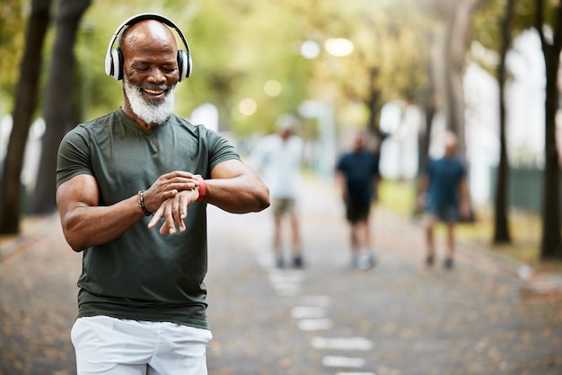 Hora de la música y correr con un hombre negro maduro mirando su reloj mientras hace ejercicio en el parque Entrena el bienestar y entrena con un atleta o corredor masculino senior que sigue su salud