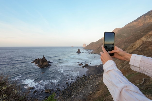 Foto hora de oro en la playa de benijo tenerife vista lateral de una mano adulta sosteniendo un teléfono inteligente