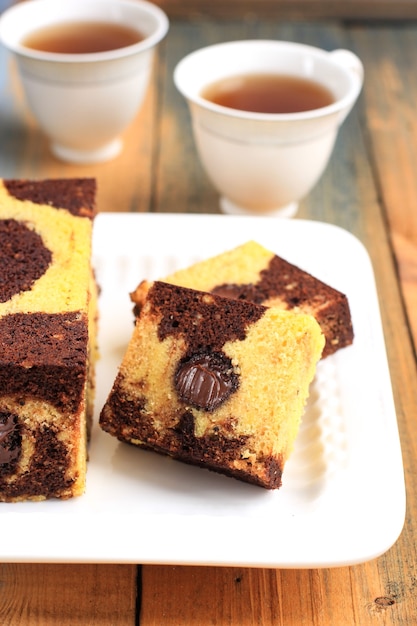 La hora del té con una rebanada de pastel de viaje de mármol, pastel cuadrado con chocolate derretido en el centro. Servido en plato blanco