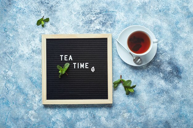 La hora del té tablero de letras negro con texto en la mesa azul con una taza de té con hojas de menta