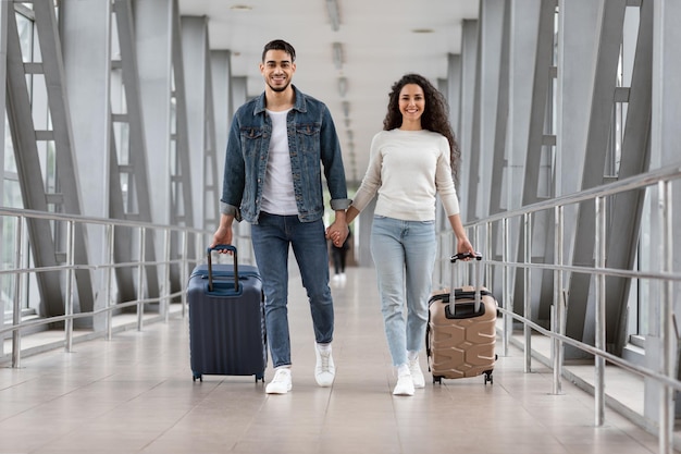 Hora de viajar alegre pareja árabe caminando con equipaje en la terminal del aeropuerto