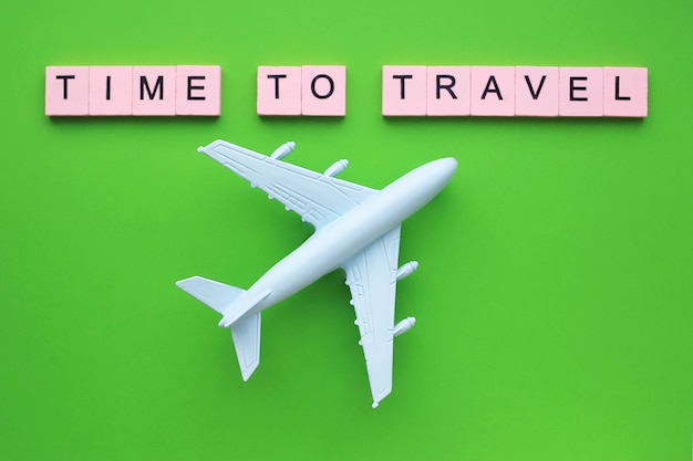 Hora de viajar palabra en bloques de color rosa y avión de juguete sobre una superficie verde