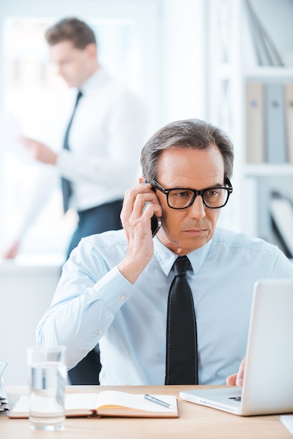 horário comercial. empresário confiante em trajes formais, trabalhando em um laptop e falando ao telefone celular