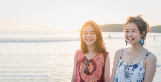 Horas de verão, retrato de duas mulheres jovens andando na praia e sorrindo.