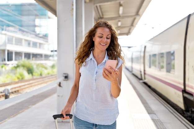 Horizontale Ansicht der Frau, die mit Smartphone auf dem Bahnsteig geht. Kaukasische Frau, die Technologie verwendet und in öffentlichen Verkehrsmitteln unterwegs ist. Reise- und Technologiekonzept.