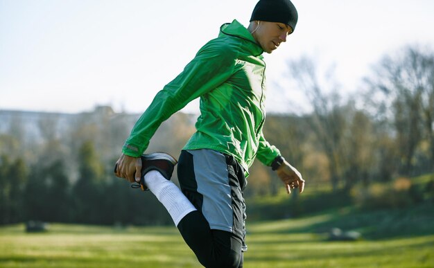 Horizontale Außenaufnahme eines jungen Sportlers, der sich im Park streckt Sportlicher gesunder Mann, der sich morgens aufwärmt Menschen- und Sportkonzept