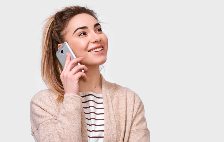 Foto horizontale innenaufnahme einer jungen hübschen frau, die lächelt und auf dem handy mit ihrer freundin spricht, die fröhlich und glücklich nach oben schaut und auf weißem studiohintergrund posiert echte menschliche emotionen