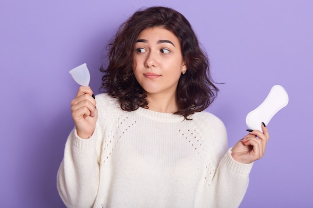 Horizontale Innenaufnahme verlegen hübsche Brünette, die Menstruationstasse betrachtet