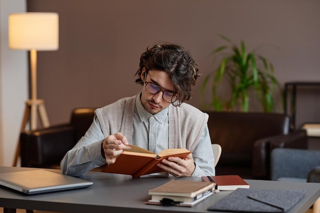 Horizontale mittlere Aufnahme eines modernen professionellen Psychologen, der in seinem Büro am Schreibtisch sitzt und Buh liest