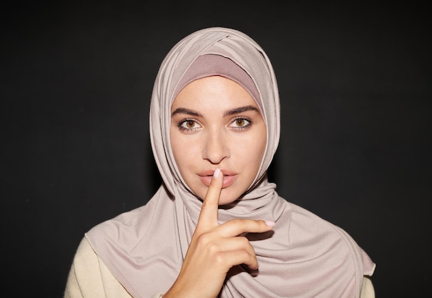 Horizontaler Kopf- und Schulterschuss einer modernen muslimischen Frau, die Hijab mit Zeigefinger über den Lippen trägt m