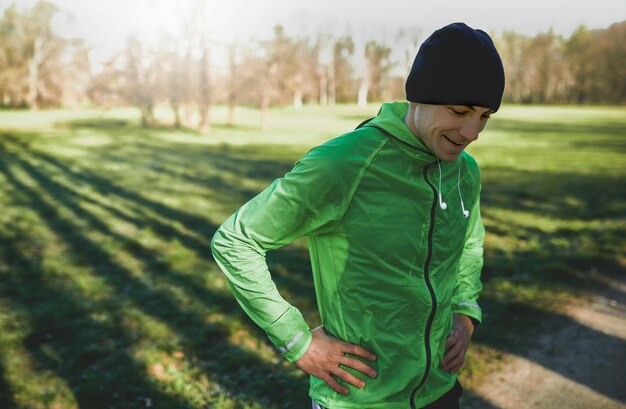 Horizontales Außenporträt eines glücklichen jungen Mannes, der nach dem Joggen draußen im Park steht Selbstbewusster junger Mann bereit zum Training