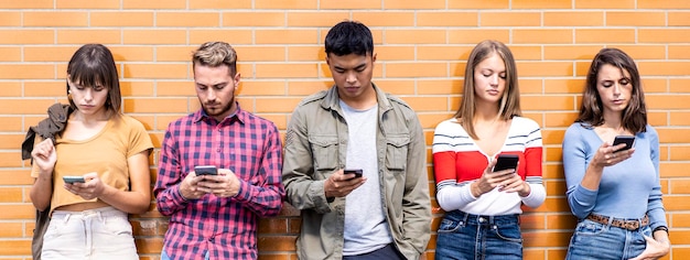 Foto horizontales banner oder vorlage mit einer gruppe multikultureller menschen, die ihr smartphone im hinterhof des universitäts-colleges nutzen. millennial-freunde, die süchtig nach mobilen smartphones sind. warmer, lebendiger filter