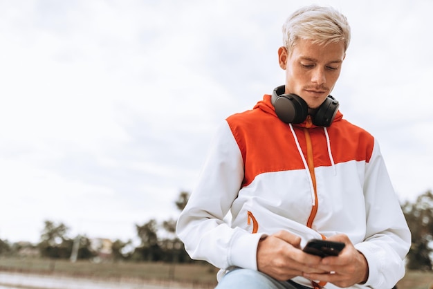 Horizontales Bild eines jungen Mannes, der eine SMS-Nachricht auf dem Smartphone im Freien im Park sendet